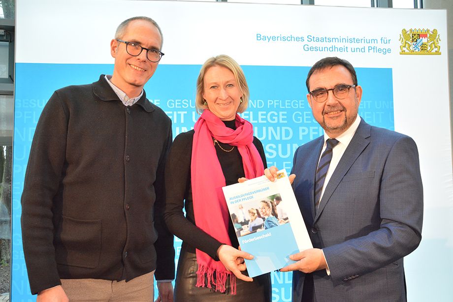 Bayerns Gesundheits- und Pflegeminister Klaus Holetschek (rechts) übergibt den Förderbescheid an Eva Faltner vom Mehrgenerationenhaus Flintsbach und Gunnar Leroy, Gesamtschulleiter der RoMed Kliniken 