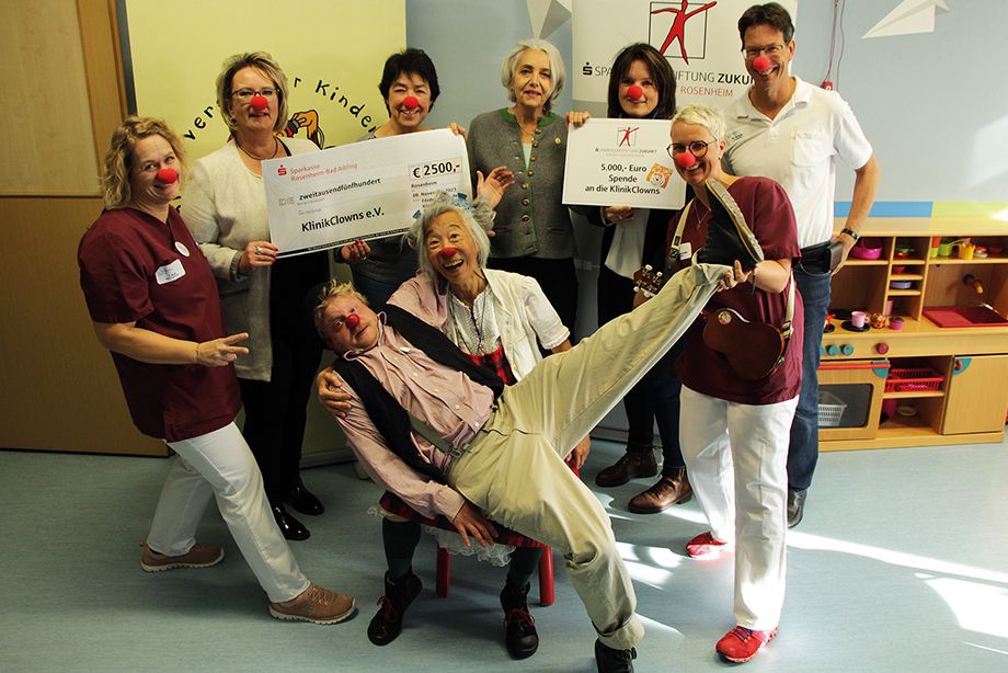 Doris Räder von der Sparkassenstiftung Zukunft für die Stadt Rosenheim (2.v.re.) sowie die Vorstandsmitglieder des Fördervereines der Kinderklinik Rosenheim, Helene Lohner (3.v.li.), und Mihaela Hammer (2.v.li.), überreichten Andrea Andrade von den KlinikClowns Bayern e.V. (mi.) die diesjährige Spende. Damit können die KlinkClowns „Muck“ und „Lulu“ (vorne im Bild) die kranken Kinder in der Rosenheimer Kinderklinik wieder ein Jahr lang aufheitern. Darüber freuen sich auch der Leitende Oberarzt Dr. Michael Buss (re.), und die stv. Stationsleitungen Sylvia Geigenscheder (Eltern-Kind-Station, vorne, re.) und Tanja Rüb (Jugend- und Kinderstation, li.) ©Sparkassenstiftung Zukunft für die Stadt Rosenheim