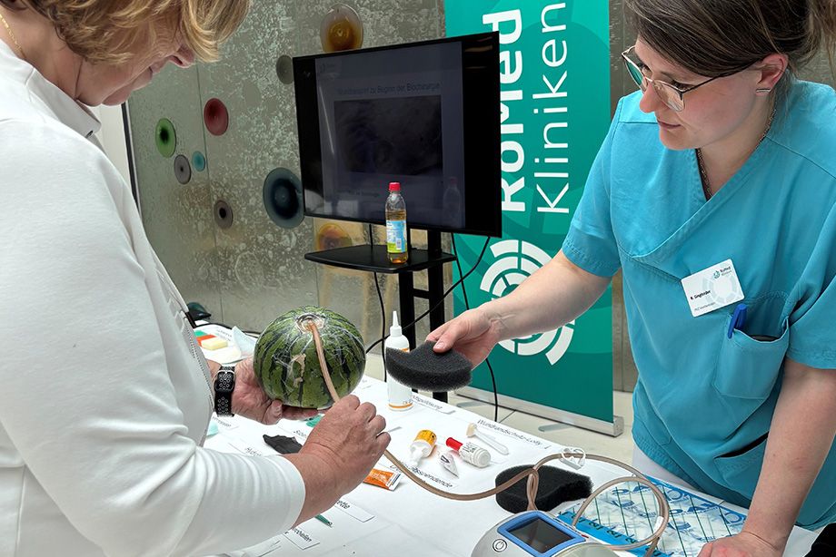 Anschauliche Demonstration: Mithilfe einer Wassermelone erklärt die Wundexpertin einer Besucherin die VAC-Therapie, bei der durch kontrollierten Unterdruck Wundsekret abgesaugt und die Wundheilung gefördert wird.
